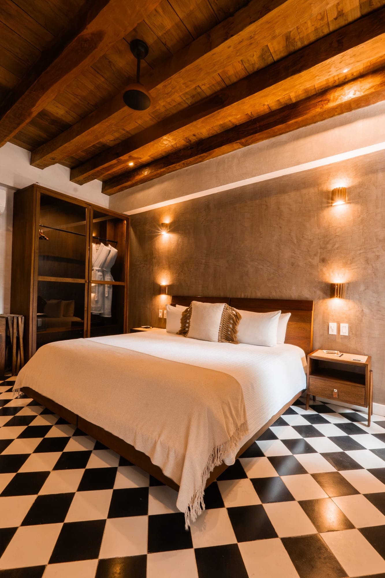 Suite con cama king, techo de vigas de madera y piso ajedrezado en blanco y negro