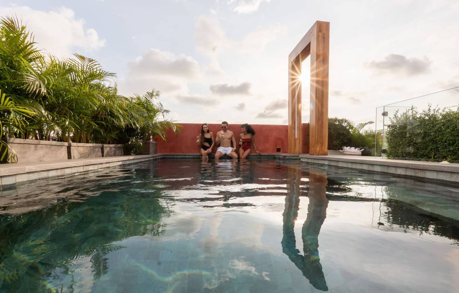 La piscina del último piso al atardecer, con el marco de madera recortado contra el sol y la ciudad al fondo